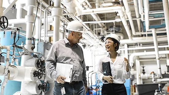 Two Ecolab experts walking and talking with clipboards in interior industrial setting.