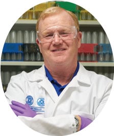 Ecolab R&D associate and food safety expert John Hanlin with arms crossed in a white lab coat and wearing PPE (gloves and protective eyewear).