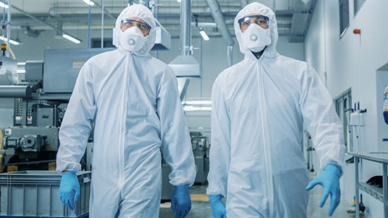 Two lab technicians walking wearing hazmat suites and masks