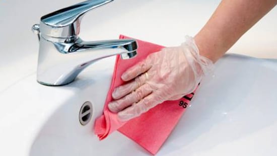 Gloved hand Scrubbing the Surface of a Sink with Surface Cleaning Products.